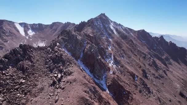 光の霞の中で雪の岩の山のピーク 青い空のドローンからの空中ビュー ピークと光のもやや急な崖 遠くにはモレーン湖が見える 古代の氷河 カザフスタン — ストック動画