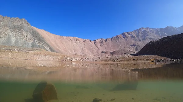 高山湖水的翡翠色 水和空气之间的边界 清澈清澈的水 附近有大石头和干草 山顶上有雪 — 图库照片