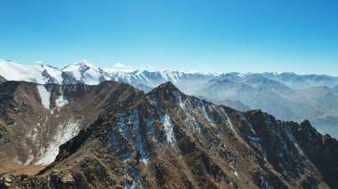 Karlı kayalık dağ tepeleri açık bir sis bulutu içinde. Mavi gökyüzünün insansız hava aracı, açık sis ve dik tepeli uçurumlar. Uzaktan bir moraine gölü görülebilir. Eski buzullar. Kazakistan