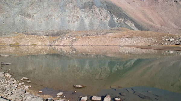 环绕着岩石的透明的山湖 水就像一面镜子 反射着岩石和斜坡 水面上的光波荡漾 底部是可见的 有很多大石头 — 图库照片