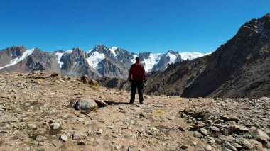 Adam dağlara ve karlı tepelere bakıyor. Yüksek dağlar mavi gökyüzüne kadar uzanıyor. Dağların zirveleri buzullarla kaplıdır. Dik uçurumlar. Büyük taşlar ve yosunlar var.