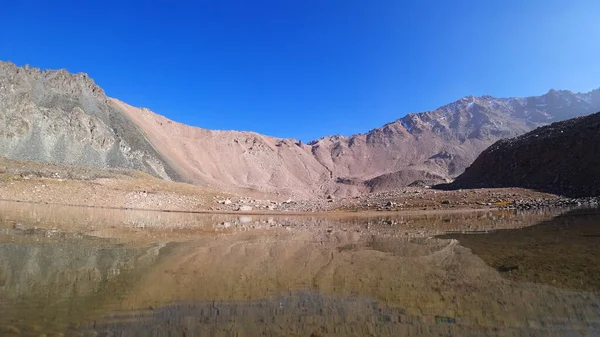 透明な山の湖の岩に囲まれた 水は鏡のようなもので 岩や斜面を反映しています 水面に光の波紋 底が見える 大きな石がある — ストック写真