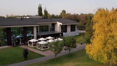 Golf parkındaki güzel ev. Sonbahar sarı-kırmızı ağaçları. Yeşil çimenlerin, tarlaların, çadırlı kafelerin üzerindeki insansız hava aracının üst görüntüsü. Düğünler, tatiller ve tatiller için bir yer. Sarı yapraklar. Gün batımı