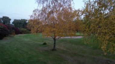 Karlı tepeler manzaralı sonbahar golf parkı. Altın ağaçların, sarı-kırmızı yaprakların ve yeşil otların hava manzarası. Evler ve dağlar uzaktan görülebilir. Gün batımı. Kazakistan