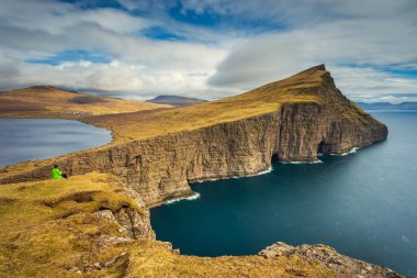 Sandavagur, Vagar, Faroe Adaları- 29 Nisan 2018: yürüyüş yolu üzerinde turistler, turistlerin turba tarlasına giden eski yol, bir Traelanipan Patikası. Köle Uçurumu manzarası. Vagar adasında bulutlu bir gün.