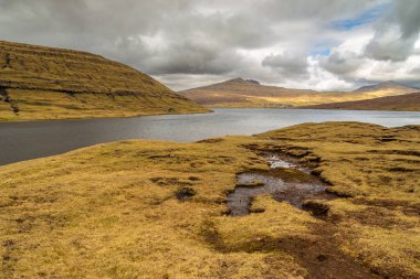 Okyanusun üzerindeki Leitisvatn Gölü manzarası. Yürüme alanı, turba tarlası, Traelanipan Patikası. Vagar adasında bulutlu bir gün. Faroe Adaları.