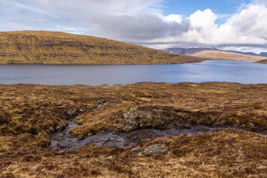 Okyanusun üzerindeki Leitisvatn Gölü manzarası. Yürüme alanı, turba tarlası, Traelanipan Patikası. Vagar adasında bulutlu bir gün. Faroe Adaları.