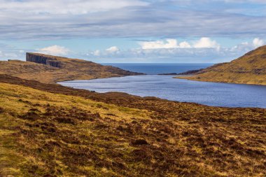 Okyanusun üzerindeki Leitisvatn Gölü manzarası. Yürüme alanı, turba tarlası, Traelanipan Patikası. Vagar adasında bulutlu bir gün. Faroe Adaları.
