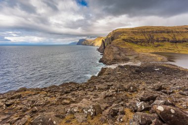 Okyanusun yukarısındaki Leitisvatn Gölü yakınındaki kıyı şeridi manzarası. Yürüme alanı, turba tarlası, Traelanipan Patikası. Vagar adasında bulutlu bir gün. Faroe Adaları.