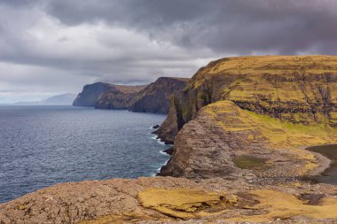 Okyanusun yukarısındaki Leitisvatn Gölü yakınındaki kıyı şeridi manzarası. Yürüme alanı, turba tarlası, Traelanipan Patikası. Vagar adasında bulutlu bir gün. Faroe Adaları.