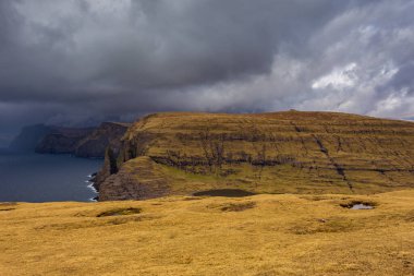 Okyanusun yukarısındaki Leitisvatn Gölü yakınındaki kıyı şeridi manzarası. Yürüme alanı, turba tarlası, Traelanipan Patikası. Vagar adasında bulutlu bir gün. Faroe Adaları.
