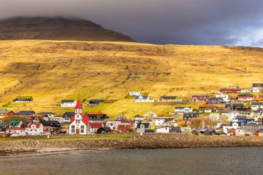 Vagar Adası 'ndaki Sandavagur kilisesinin manzarası. Bir tepenin yamacında küçük bir köy. Faroe Adaları.