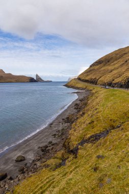 Vagar adasındaki sahil boyunca uzanan yol manzarası. Dağ manzarası. Vagar Adası 'nda bir otobüs. Faroe Adaları.