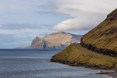 Vagar adasındaki sahil boyunca uzanan yol manzarası. Dağ manzarası. Vagar Adası 'nda bir otobüs. Faroe Adaları.