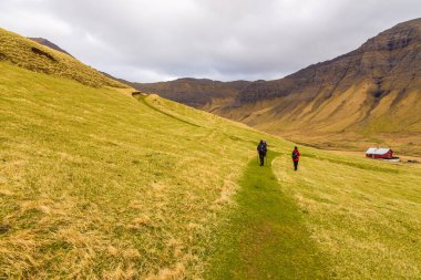Gasadalur, Faroe Adaları - 30 Nisan 2018: Küçük Gasadalur köyü yakınlarındaki Vagar adasında yürüyüş yolu üzerinde turistler. Bulutlu bahar günü.