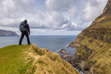 Gasadalur, Faroe Adaları - 30 Nisan 2018: Küçük Gasadalur köyü yakınlarındaki Vagar adasında yürüyüş yolu üzerinde turistler. Bulutlu bahar günü.
