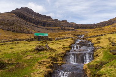 Faroe Adaları 'ndaki volkanik takımadaların bir parçası olan Bordoy Adası' ndaki dik bir dağ yamacından akan bir şelale..