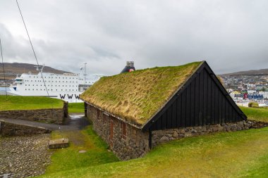 Thorshavn, Faroe Adaları, Danimarka - 03 Mayıs 2018: Thorshavn 'daki Skansin kalesinde çatısı olan taş bina. Arka planda feribot ve deniz feneri var..