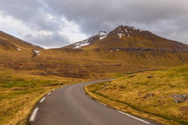 Streymoy adasındaki tepeler boyunca asfalt yol. Vadideki bulutlar. Eidi, Faroe Adaları, Danimarka.