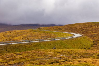 Streymoy adasındaki tepeler boyunca asfalt yol. Bulutlu bir gün. Faroe Adaları, Danimarka.