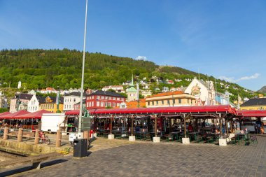 Bergen, Norveç - 27 Mayıs 2018: Limanın yanındaki şehir merkezinde restoranları olan balık pazarı. Renkli konutlar ve arka planda yeşil tepeler.