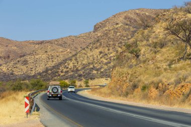 Khomas, Namibya - 28 Eylül 2018: Arabalar yolda. Otoyol boyunca Namibya manzarası. Tepeler ve Afrika bitkileri..
