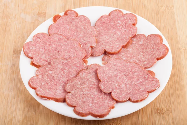 Sliced sausage on a white plate on wood — Stock Photo, Image