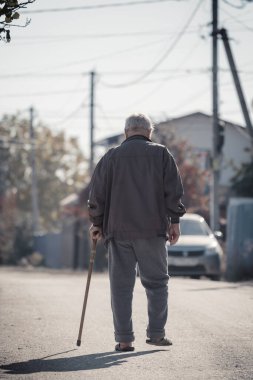 Saratov, Rusya - 10.10.2021: Sopalı yaşlı bir adam yol boyunca yürüyor. Yalnız büyükbaba. Arka plan.