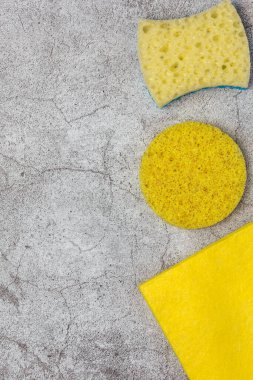 Temizlik konsepti. Ev eşyaları paçavraları, peçeteler, çamaşır tozunu silmek için çeşitli sarı süngerler ve fotokopi alanı olan boş bir arkaplanda ev işleri üst görünümü.