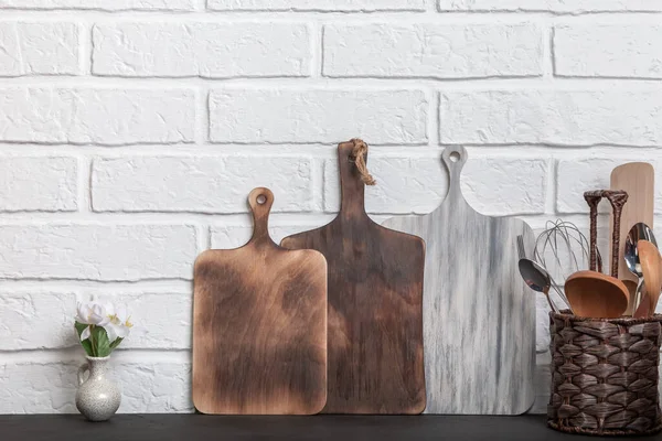 台所用品、カトラリー、食器類、白いレンガの壁の背景の正面ビューに木製のまな板 — ストック写真
