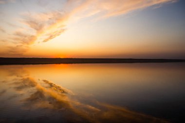 Gölde yansıması olan güzel bir gün batımı, kanat şeklinde kıvrımlar. Sakin su, yatay çekim.