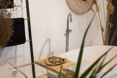 Küvetli ve musluklu modern banyo. Panoramik sabun ve temiz havlu manzarası, bitki süslemeleri ve mumlar. Lüks banyo, iç tasarım konsepti..