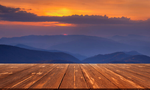 Autumn beautiful background with sunset over mountains and empty wooden table in nature outdoor. Natural template landscape.