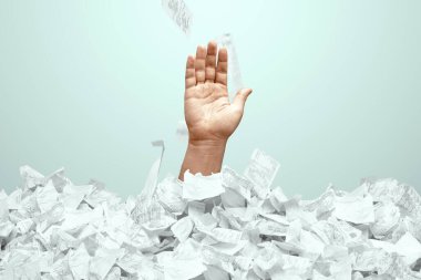 Bir adamın eli çek ve faturalardan oluşan bir dağdan sarkıyor. Bir adam borç, kredi, ipotek, kredi, ipotek içinde boğuluyor