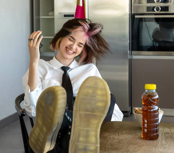 happy woman shaking her head from side to side, reclining in her chair with her feet on the worktop, horizontal indoor picture