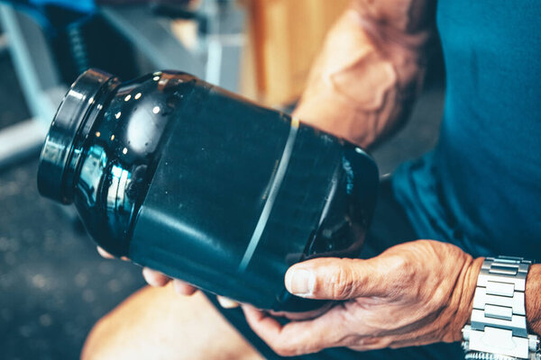 Stock photo of a detail of a protein bottle in the hands of a muscular man in the gym. Fitness and sports