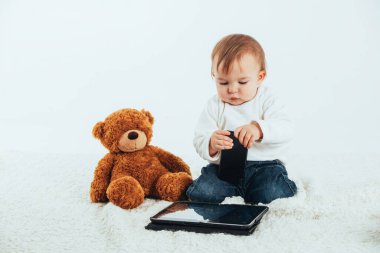 Yanında oyuncak ayı olan bir tabletin ekranına bakan bir bebeğin beyaz arkaplanlı resmi..