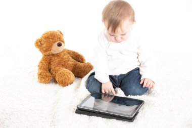 Yanında oyuncak ayı olan bir tabletin ekranına bakan bir bebeğin beyaz arkaplanlı resmi..