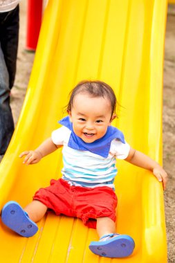 Çocuk sarı bir kaydırak ile oynuyor. Parkta gülümsüyor..