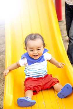 Çocuk sarı bir kaydırak ile oynuyor. Parkta gülümsüyor..