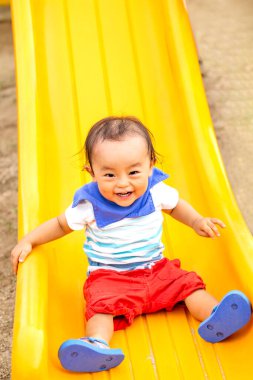 Çocuk sarı bir kaydırak ile oynuyor. Parkta gülümsüyor..