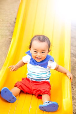 Çocuk sarı bir kaydırak ile oynuyor. Parkta gülümsüyor..