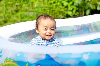 Oğlan yazın ortasında sıcak bir günde evde havuz başında mutlu mesut oynuyor. Gülümsemenin güzel çocuğu..