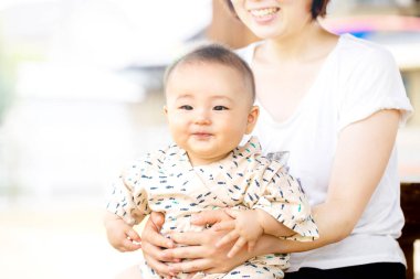 Güzel, genç bir anne dışarıda bir bankta bebeği dizlerinin üstünde tutuyor. Bebek gülümseyerek kameraya bakıyor..
