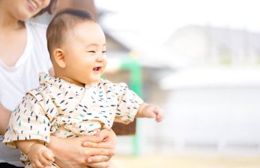 Güzel, genç bir anne kucağında bebeği dışarıda tutuyor. Bebek eğlenceli görünüyor..