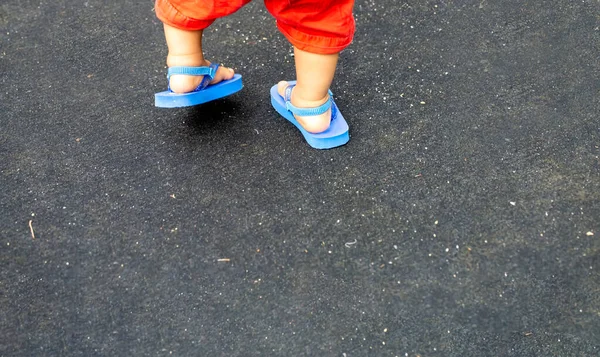 Stopy Dziecka Czerwonych Spodniach Niebieskich Sandałach Plażowych Czarnym Tle Przestrzeni — Zdjęcie stockowe