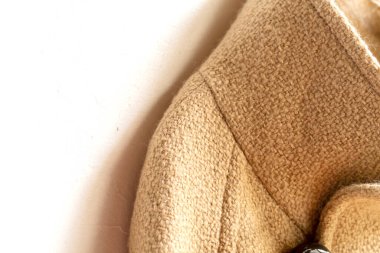 Elbiselerde asılı bej renkli yün palto. Beyaz arka planda asılı. Kapat..