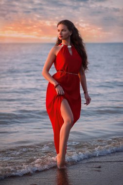 Gün batımında deniz kıyısında uzun kırmızı elbiseli bir kadın.