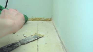 Yüzeyi süpürgelik tamiri için hazırlıyorum. Yapıştırıcı tabancası ve duvarla zemin arasında delik açan spatula ile yakın plan kadın işçi eli.