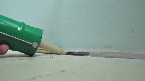 Orta yaşlı kadın elinin duvar ve zemin arasındaki deliği yapıştırıcı ile kapatması. — Stok video